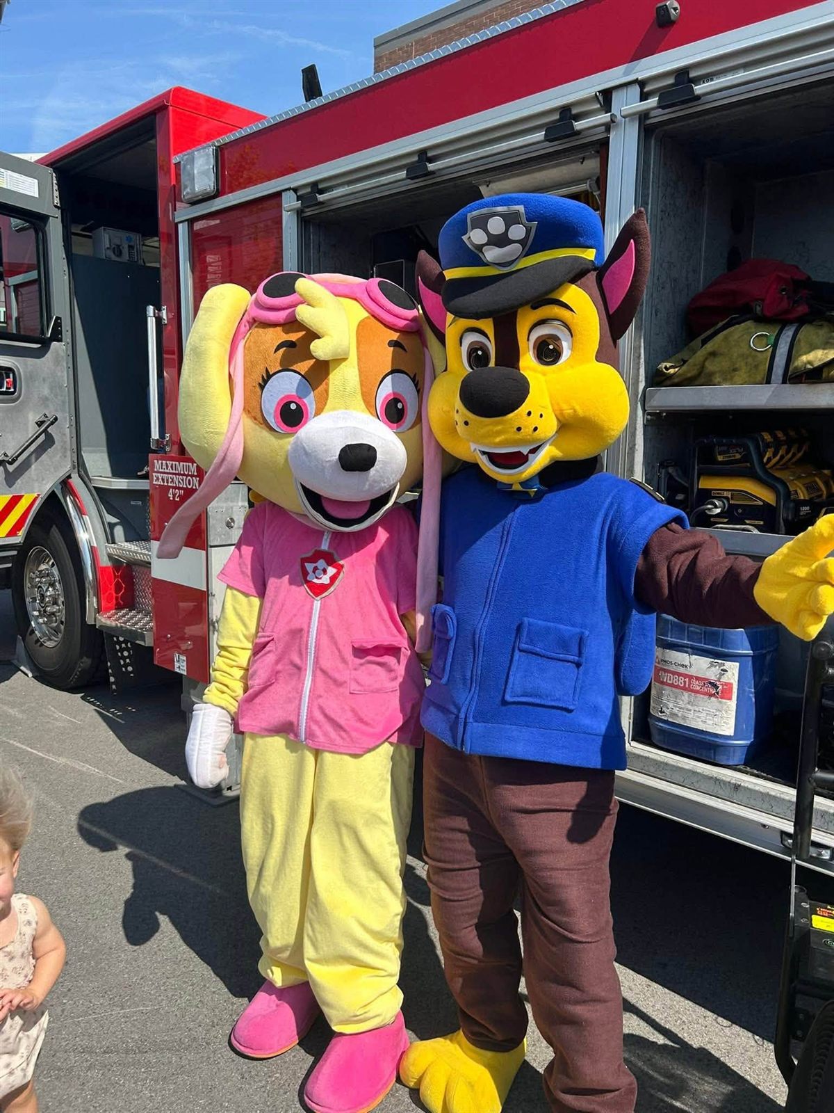 Two rescue-pup mascot performers posing beside a real fire truck at a kids' community event