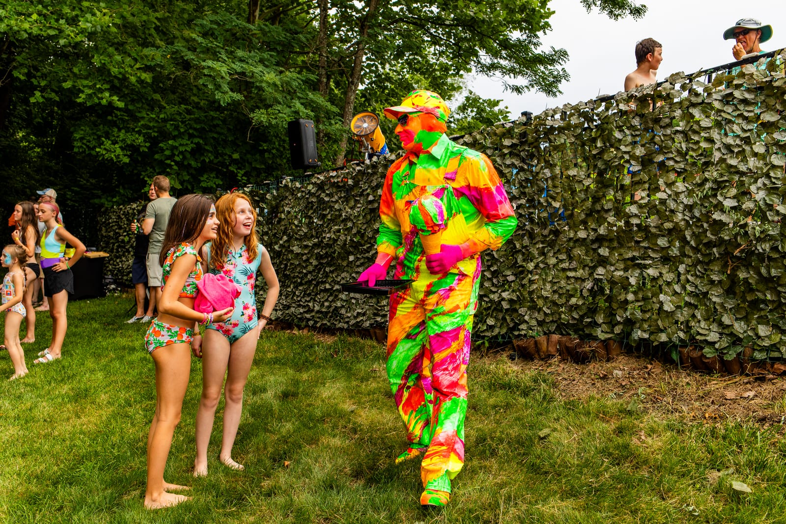 Costumed performer in a vivid neon suit walking toward guests across a lawn