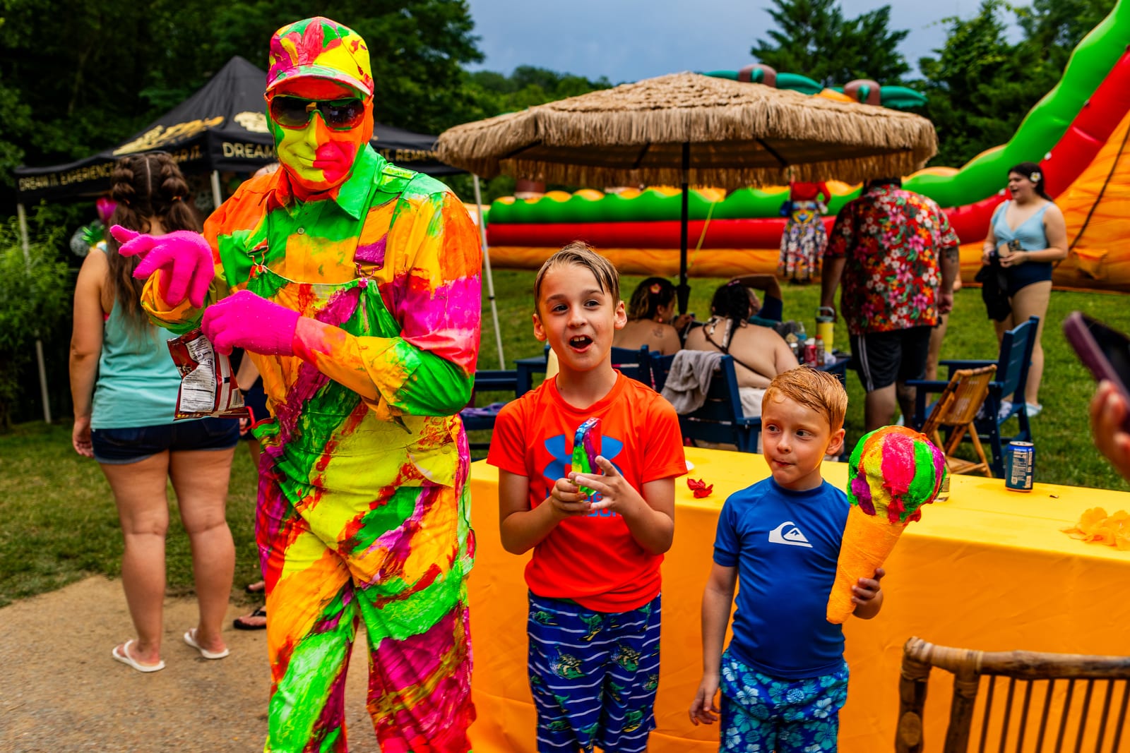 Performer in a neon suit handing toys to young guests beside an inflatable slide