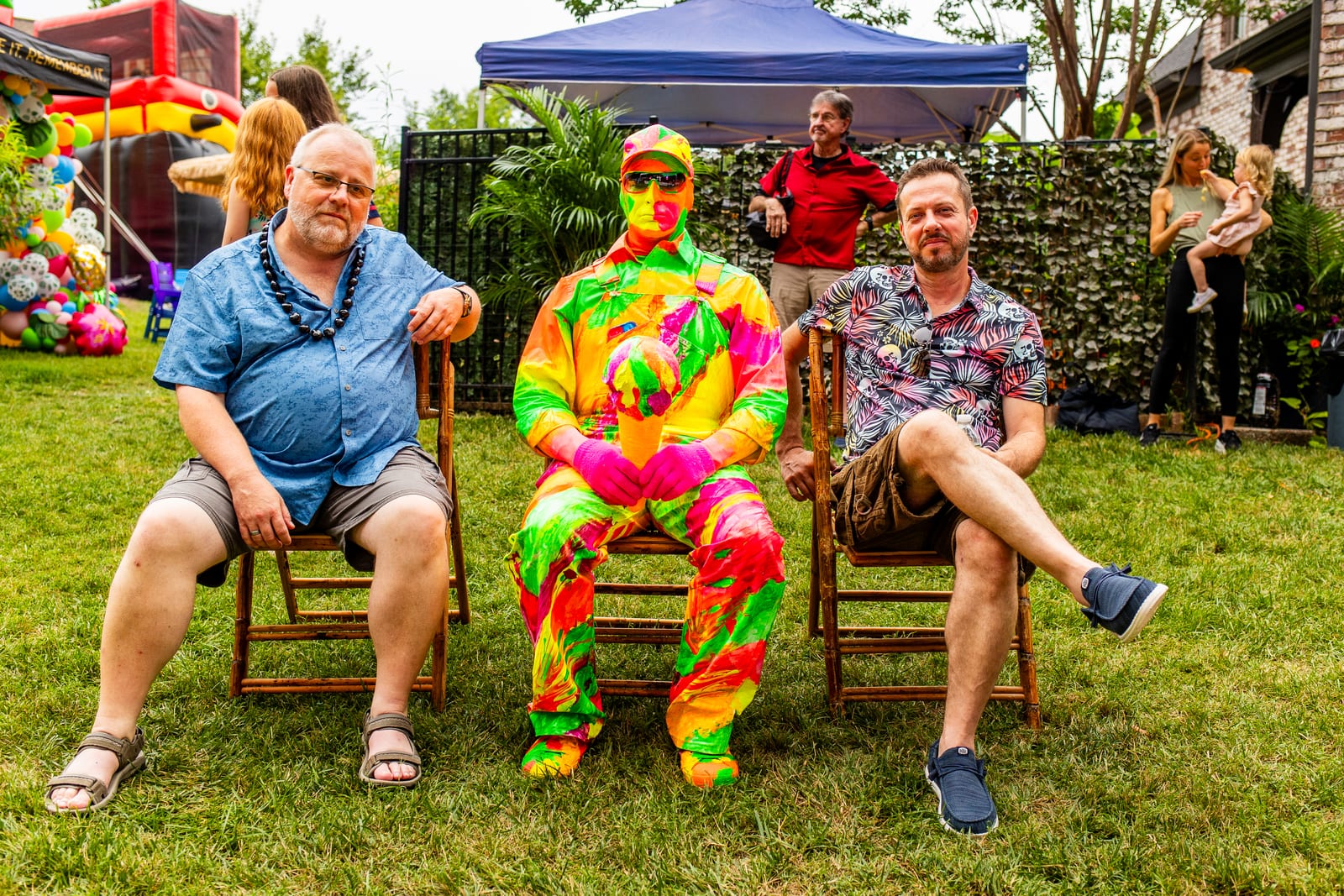 Two seated guests posing either side of a performer in a vivid neon costume