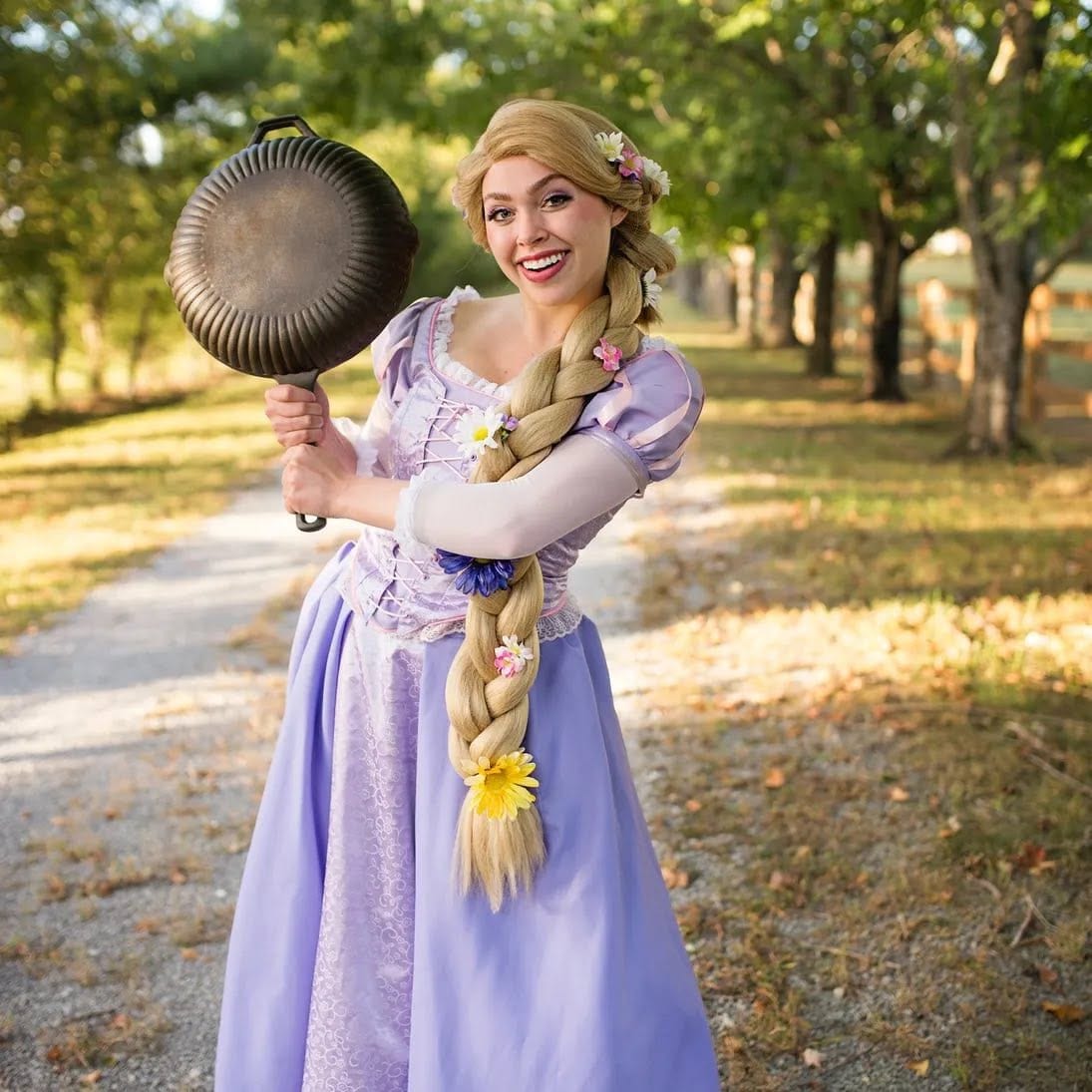 Long-braided princess character in a lavender gown holding a frying pan on a tree-lined path. Character Meet & Greets by EPIC Parties in Middle Tennessee.
