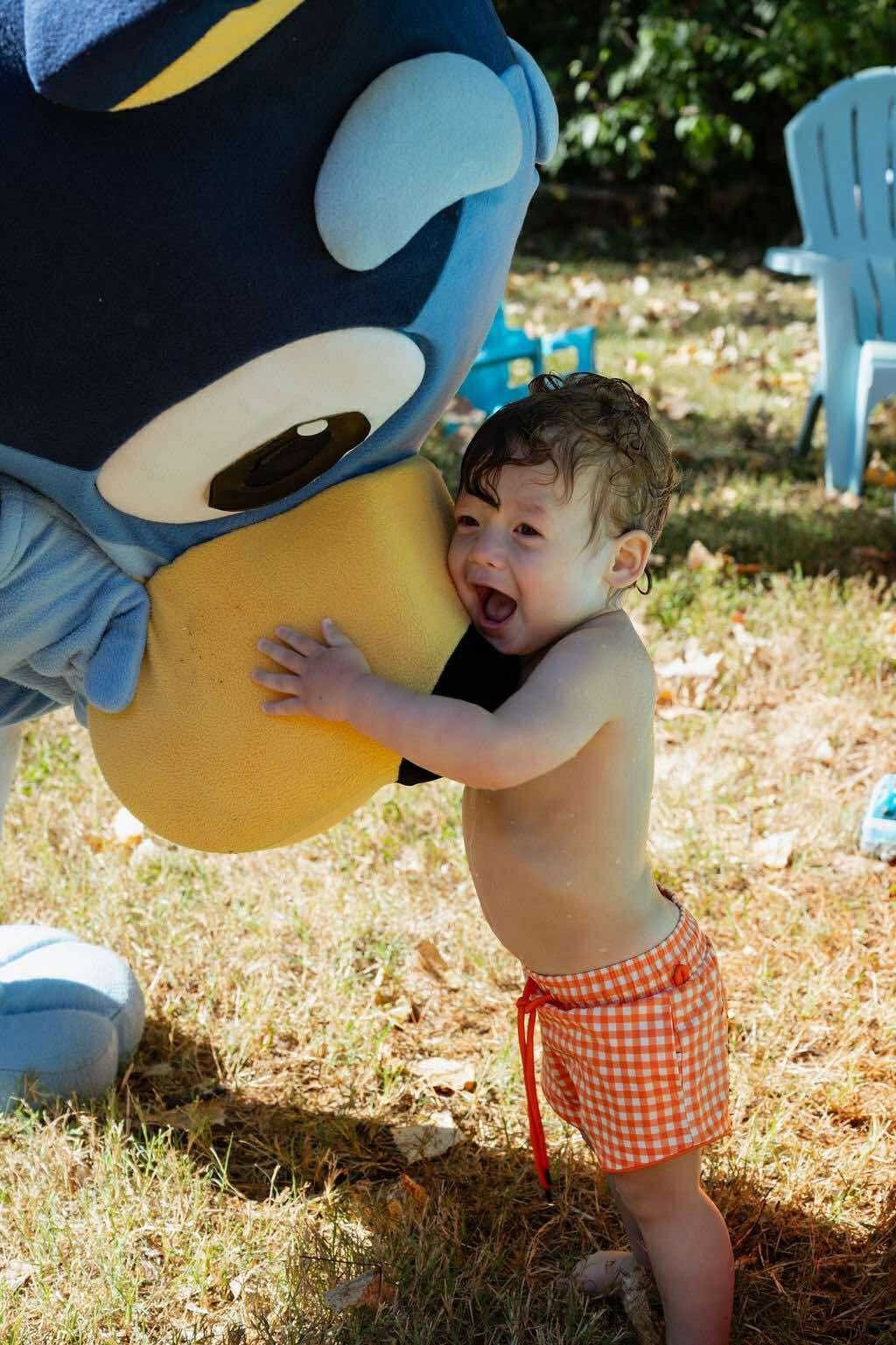 Blue cartoon-dog mascot performer greeting a toddler on a lawn