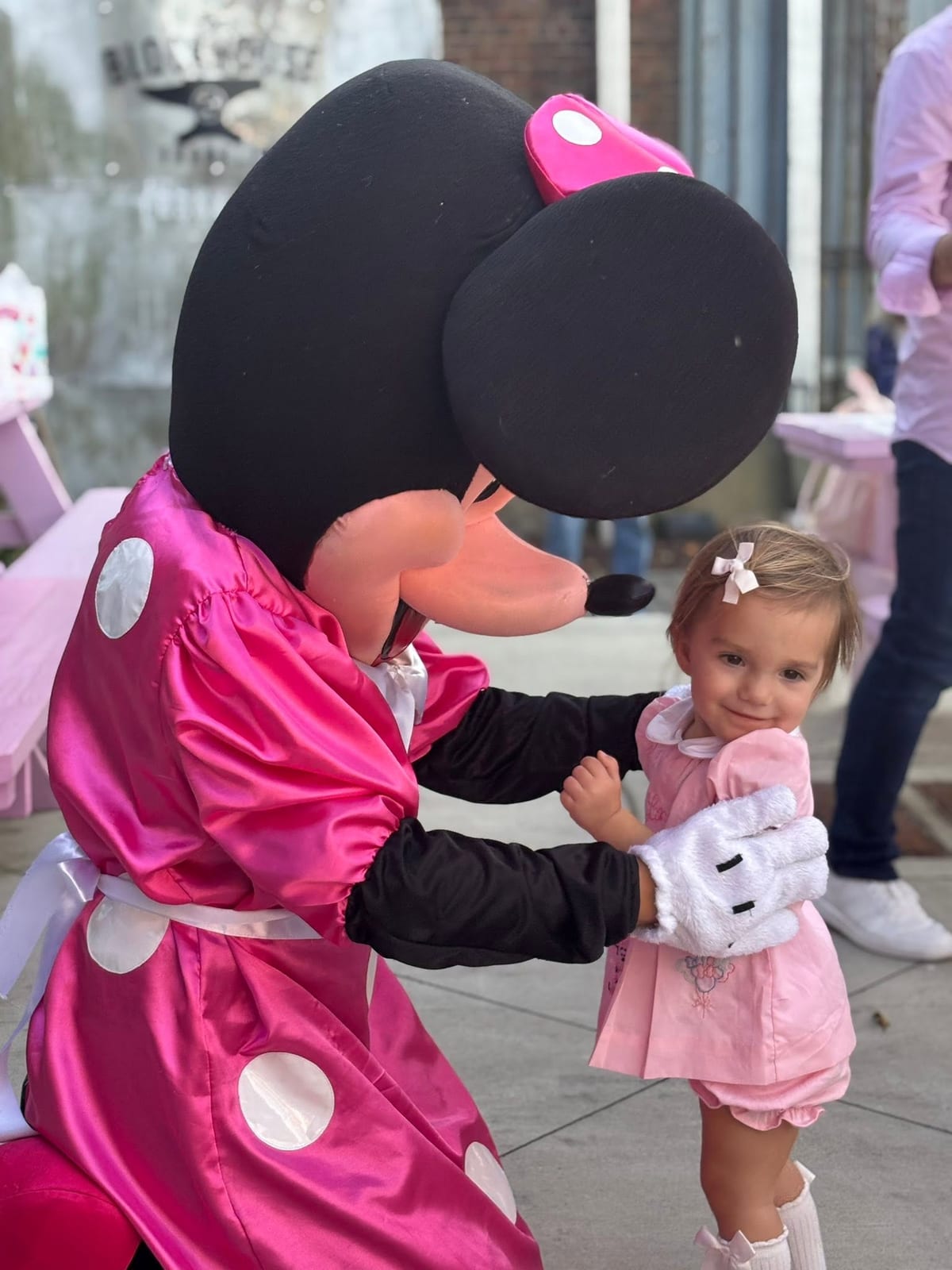 Mouse mascot in a pink polka-dot dress holding hands with a small child
