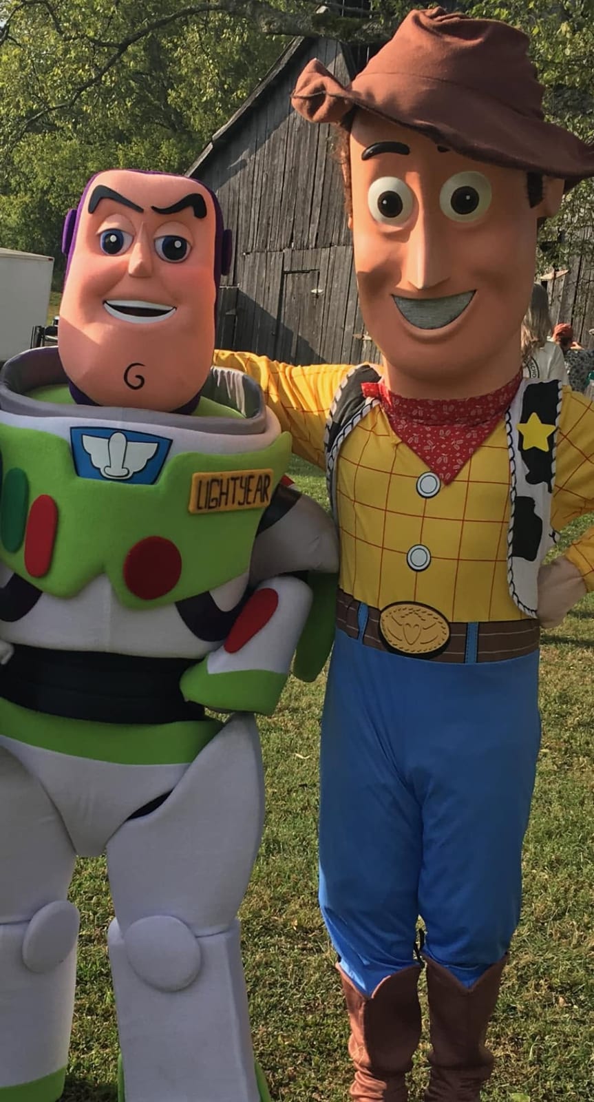 Space-ranger and cowboy toy mascots standing together outdoors at a farm party