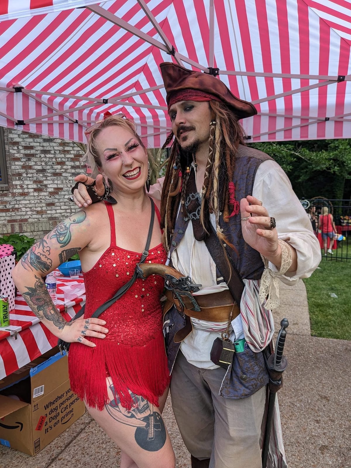 Pirate captain character and a red-sequinned performer posing under a striped canopy