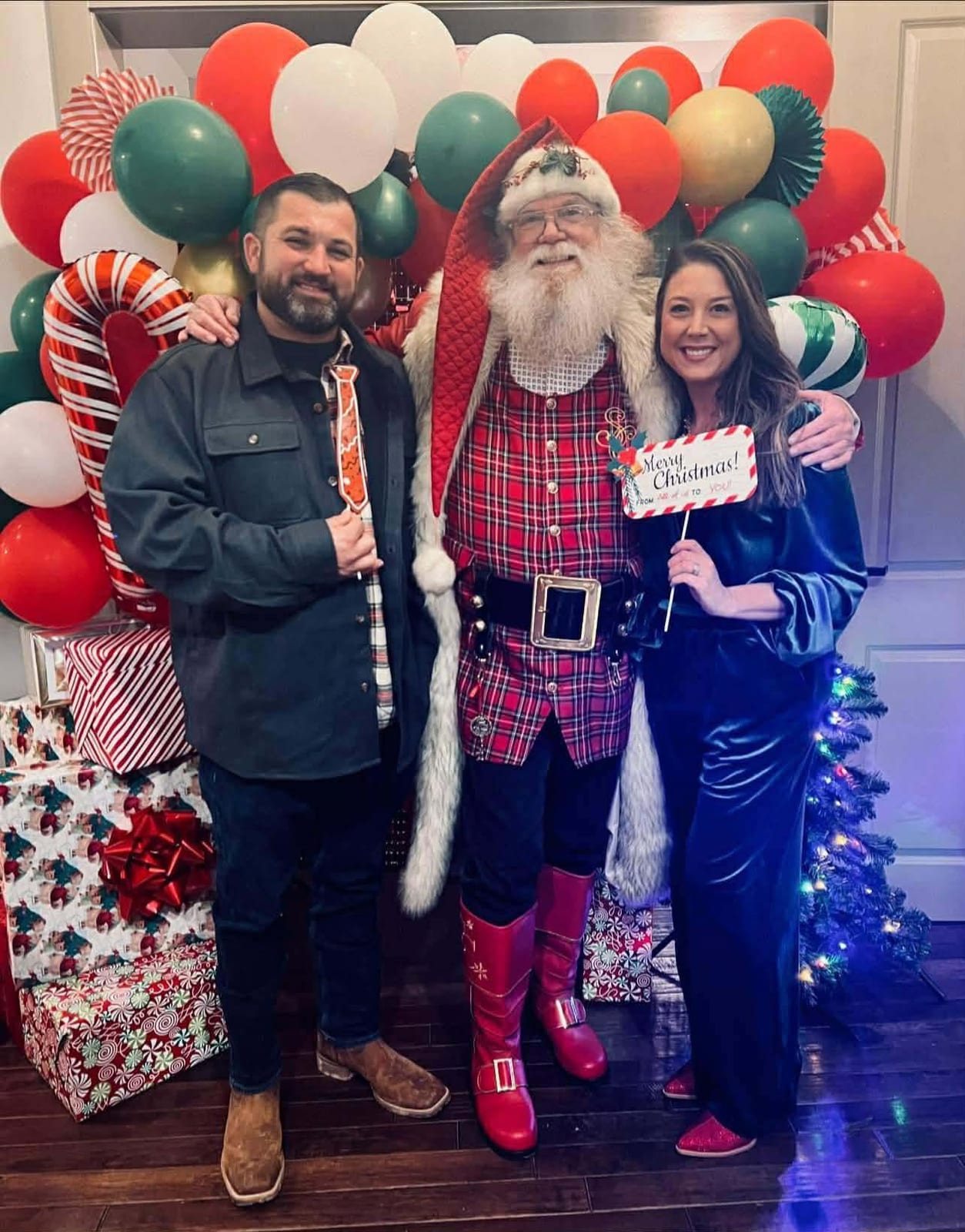 Santa Claus posing with two guests in front of a red and green balloon garland