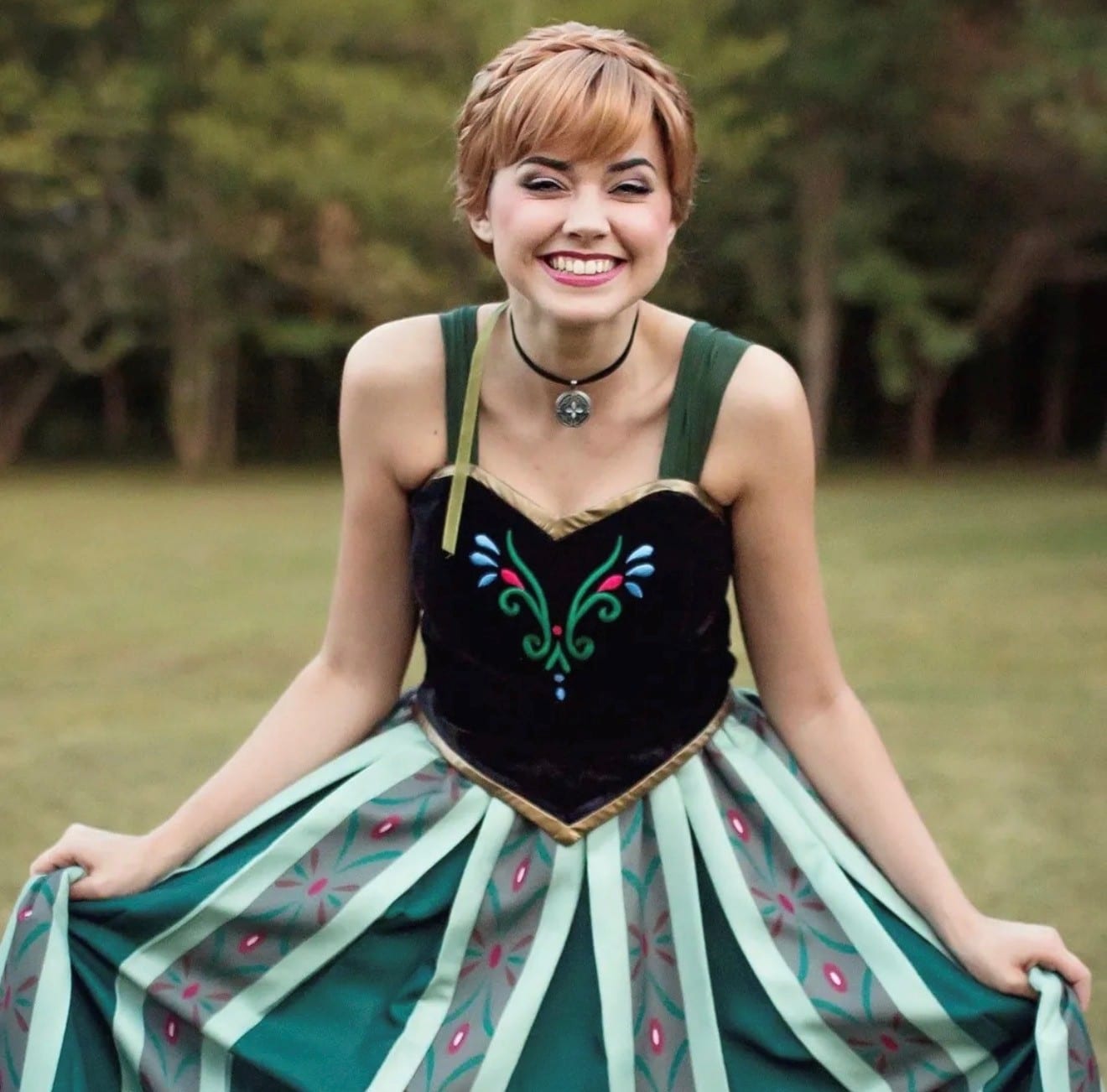 Princess character in a green and teal coronation gown holding out her skirt on a lawn