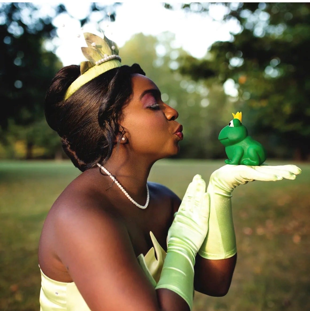 Princess character in a yellow gown, tiara and long gloves holding a small crowned toy frog