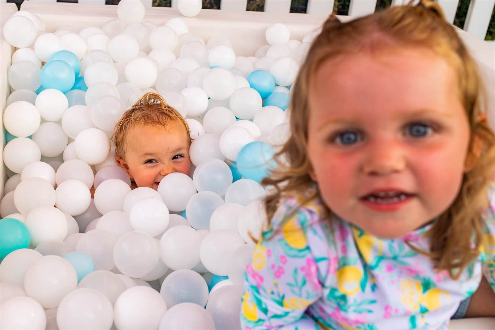 Two smiling toddlers playing in a soft-play ball pit filled with white and pale blue balls