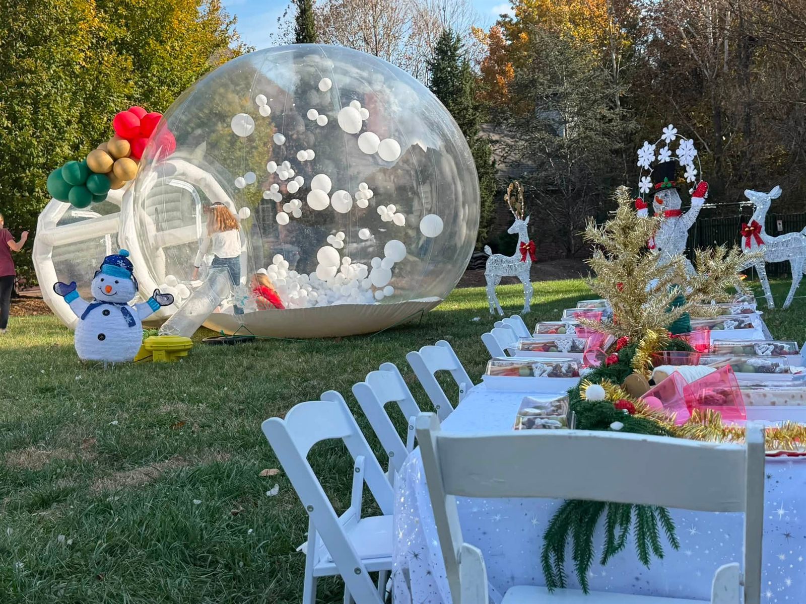 Winter bubble tent with snowman balloons, reindeer figures and a decorated dining table on grass