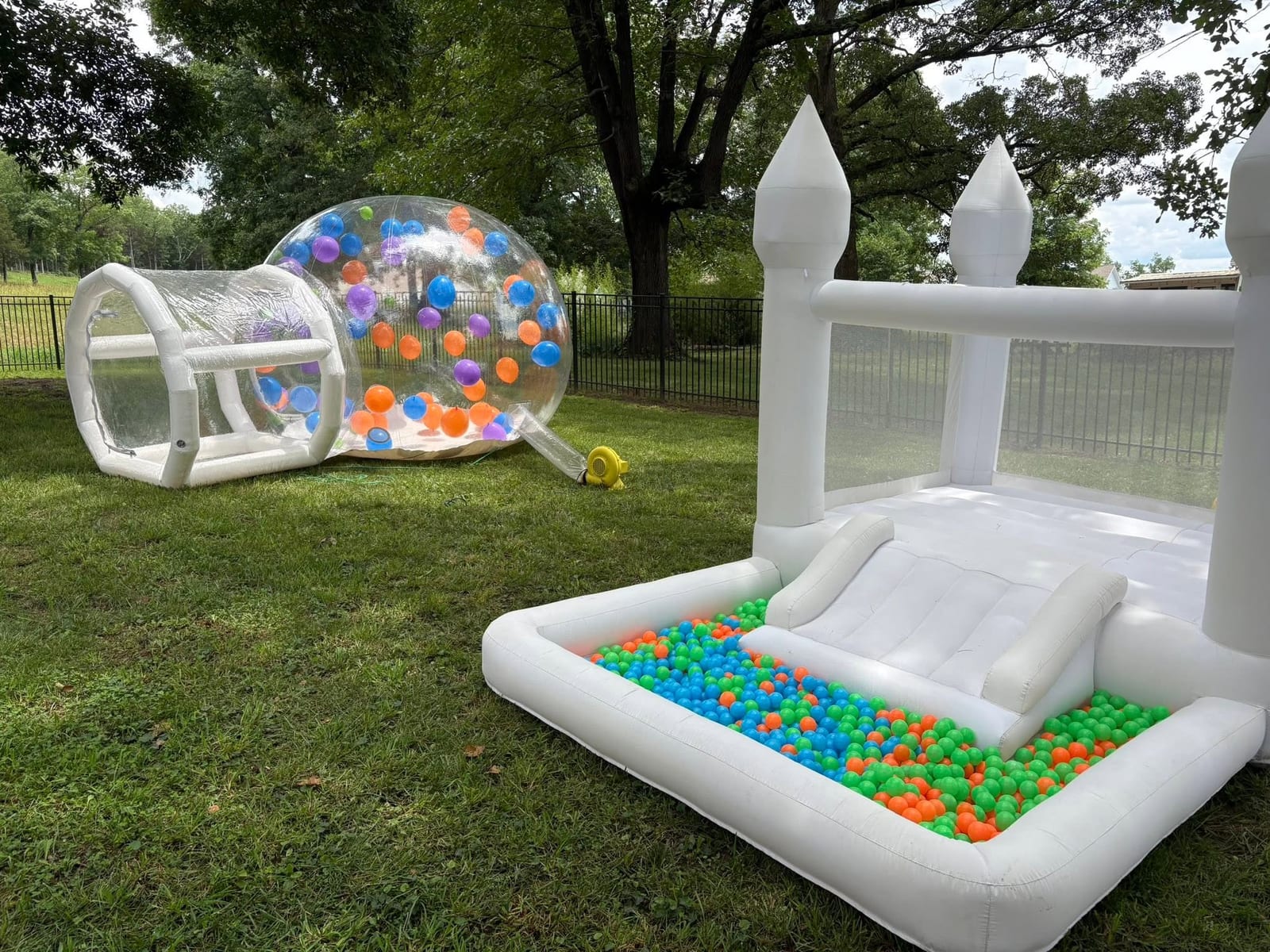 Inflatable clear bubble tunnel, white bounce house and a ball pit set up on a lawn