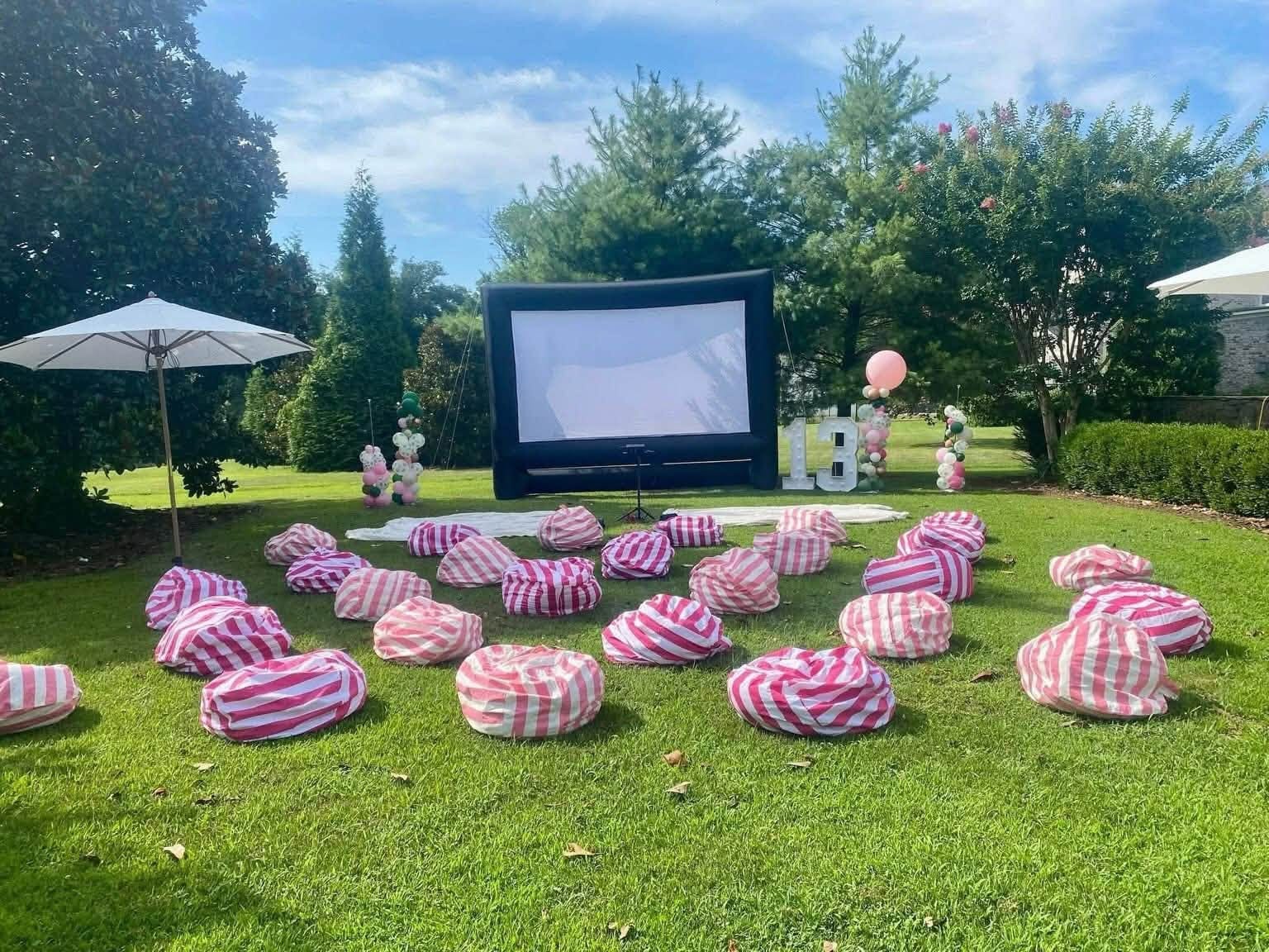 Large inflatable outdoor movie screen on a lawn with pink striped bean bags arranged in front