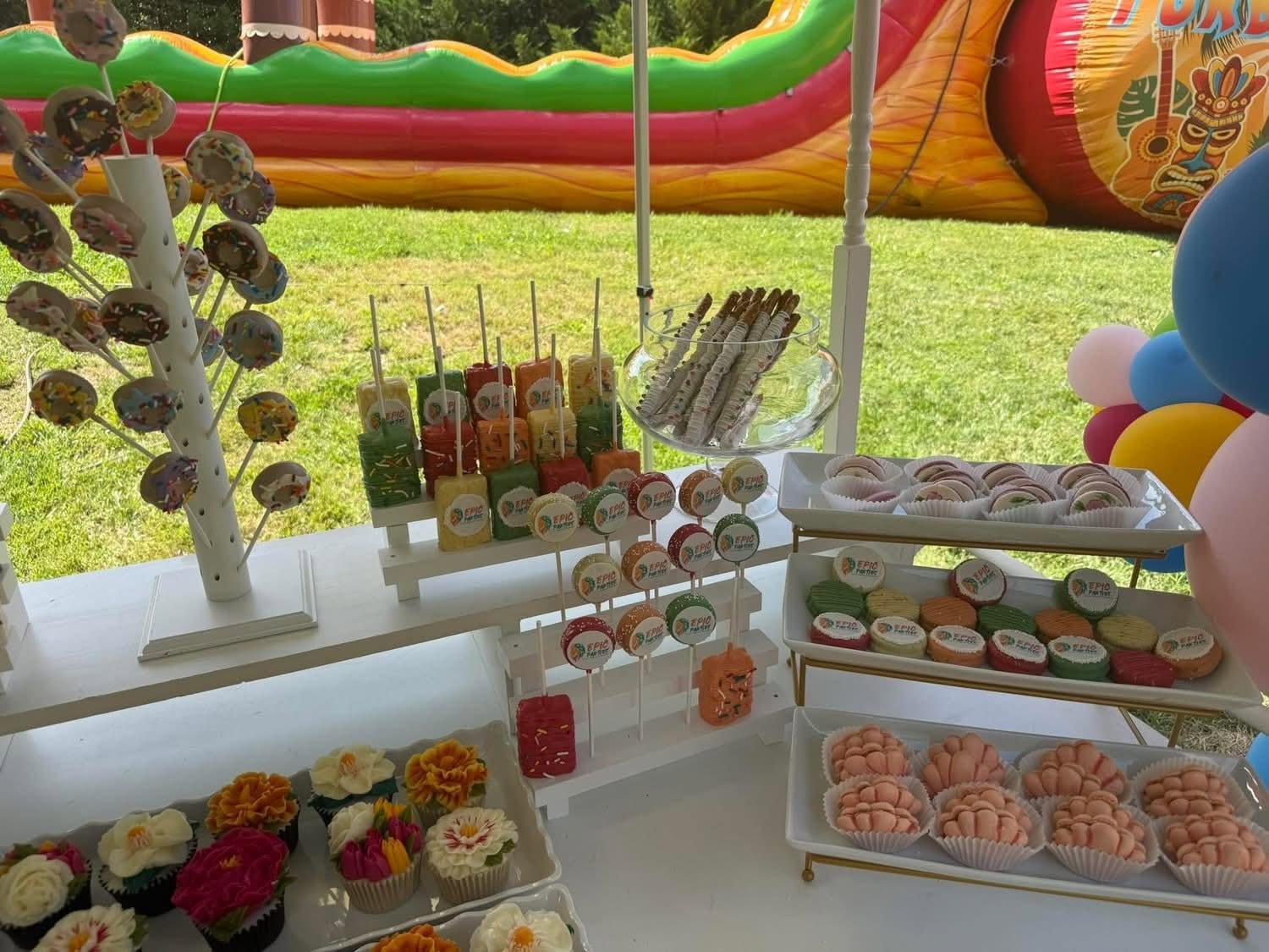 Outdoor dessert cart of cake pops, mini desserts and cupcakes beside a colourful inflatable slide