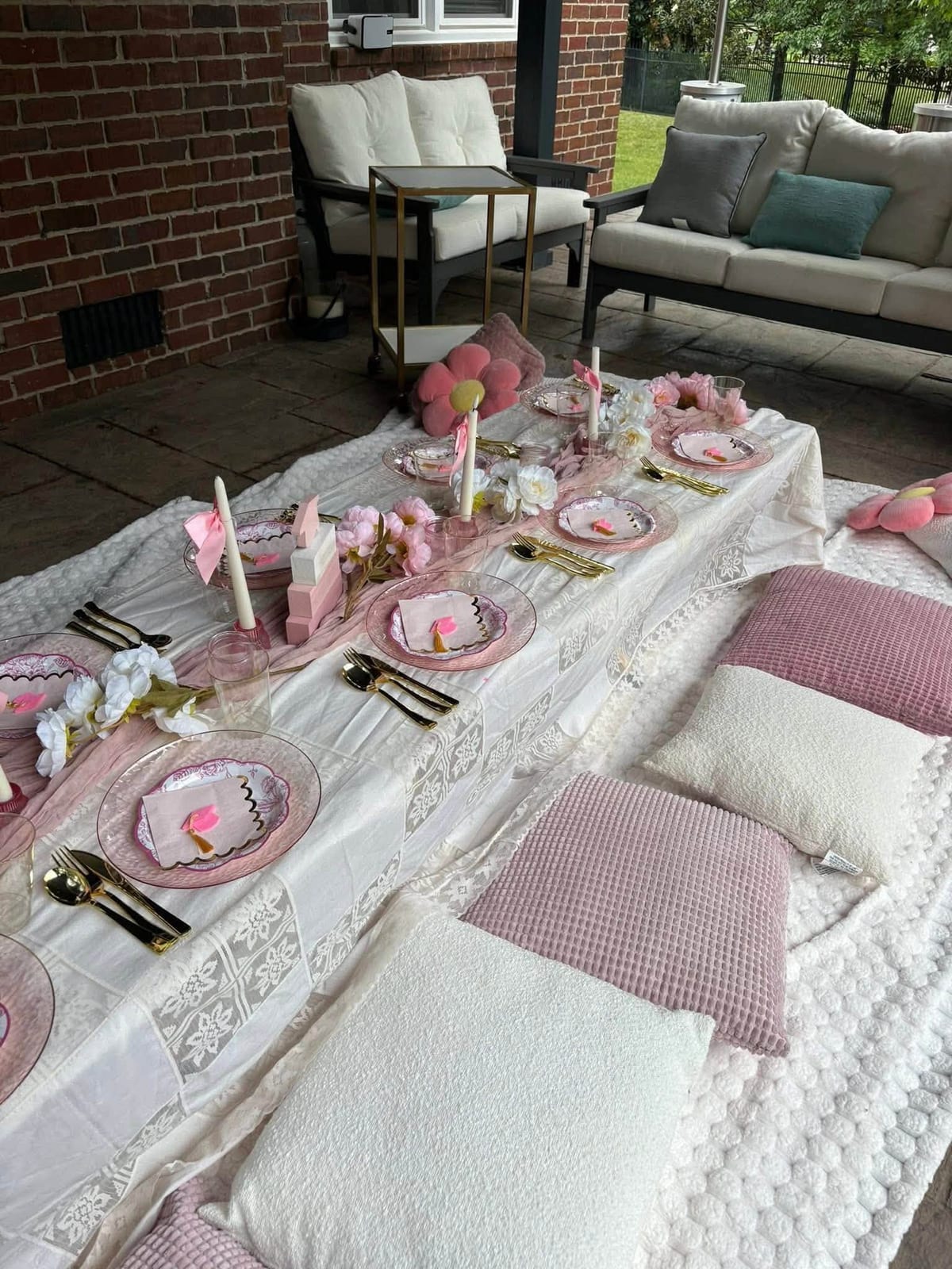 Low floor-picnic table styled in pink and cream with cushions, lace runners and place settings on a patio