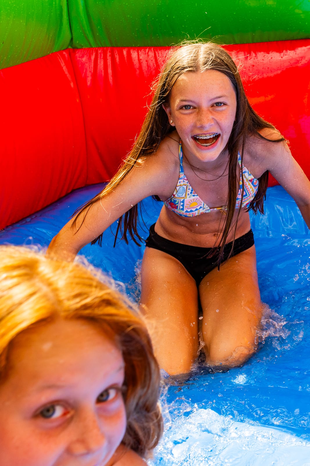 Two young guests laughing at the bottom of an inflatable water slide