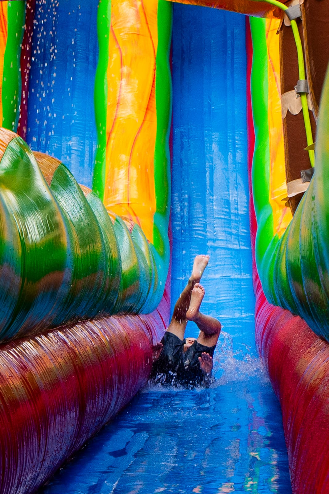 Child mid-descent on a tall rainbow inflatable water slide