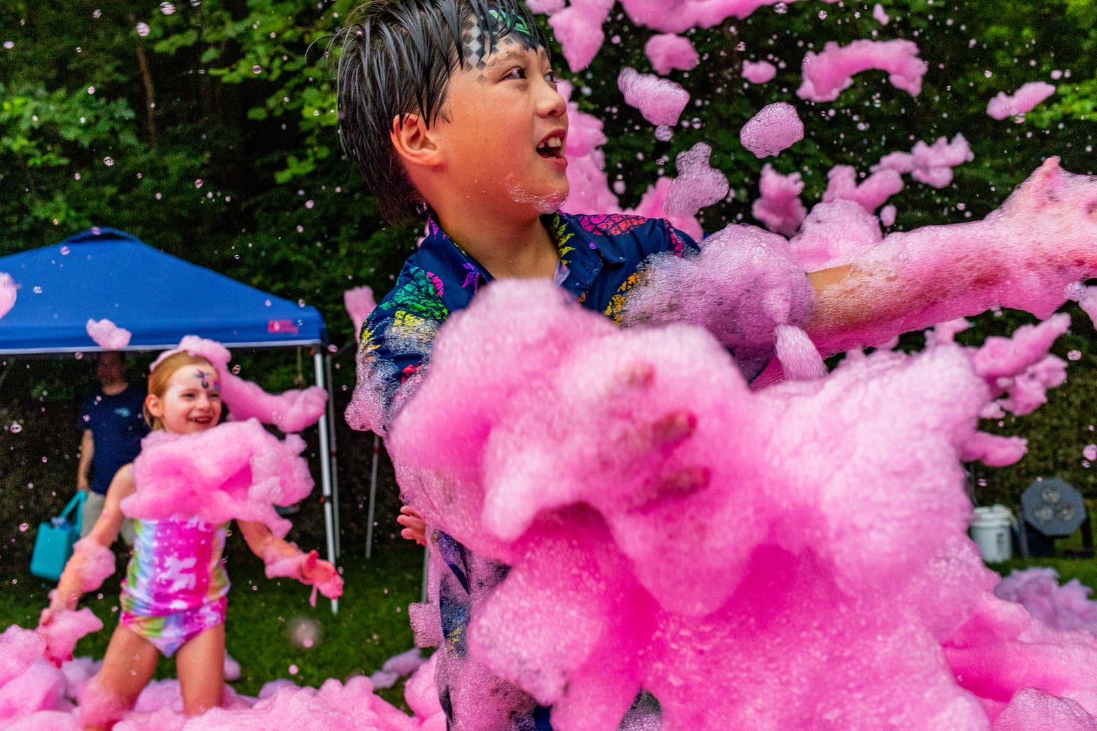 Children playing in clouds of bright pink party foam on a lawn