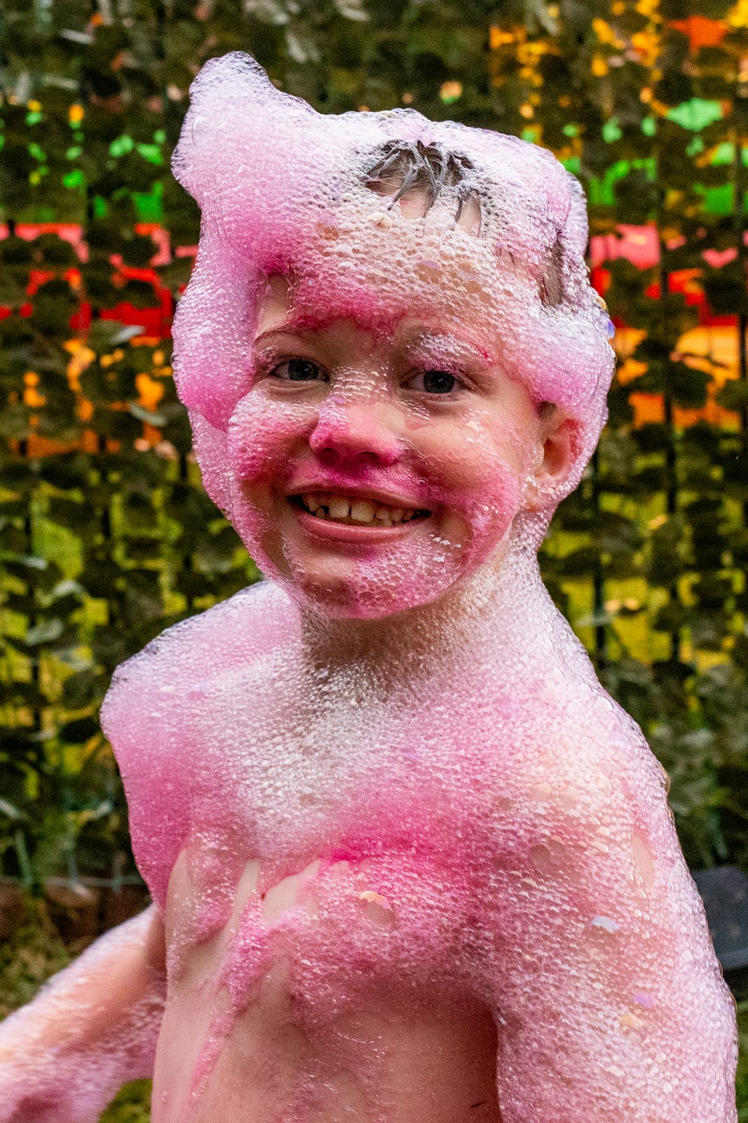 Child covered in pink party foam wearing a foam crown and grinning