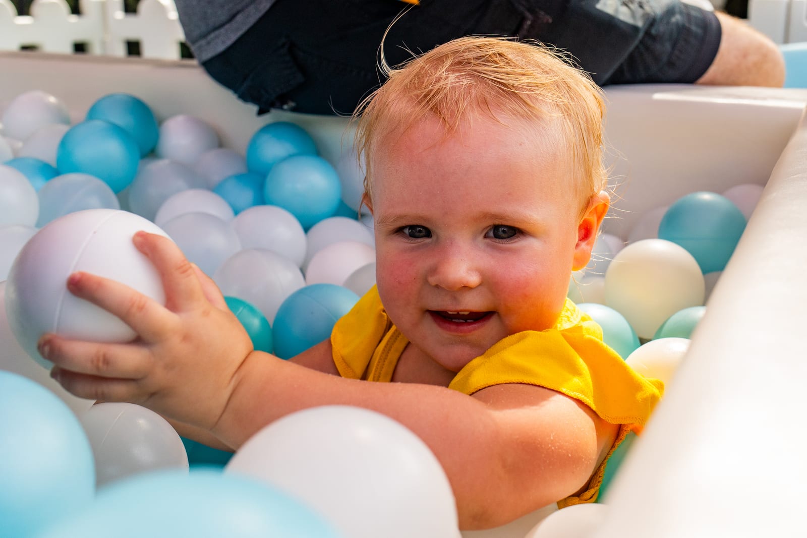 Baby holding a ball and smiling in a pastel blue and white ball pit