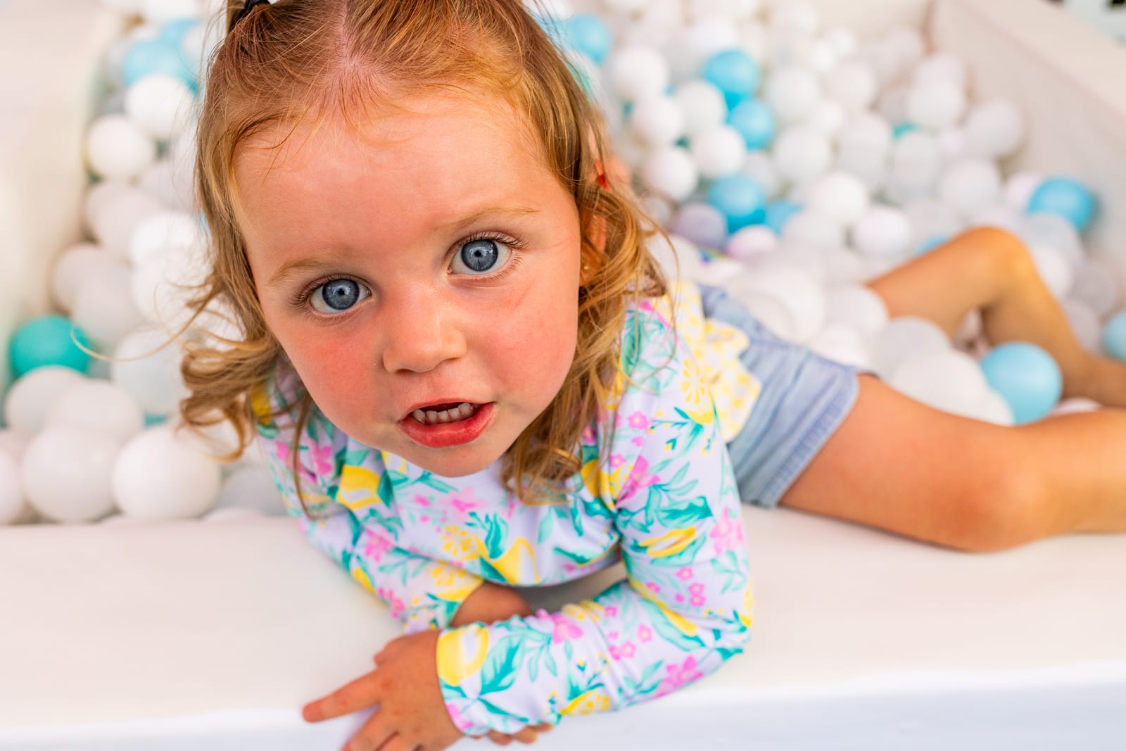 Toddler lying in a white and blue ball pit looking up