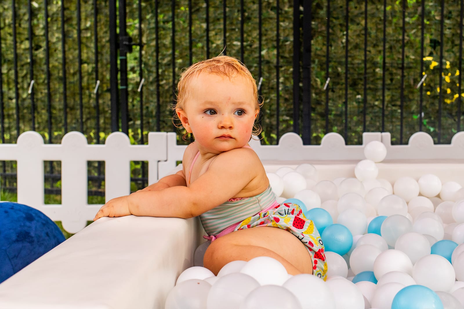 Baby leaning on the edge of a white ball pit at an outdoor soft-play area