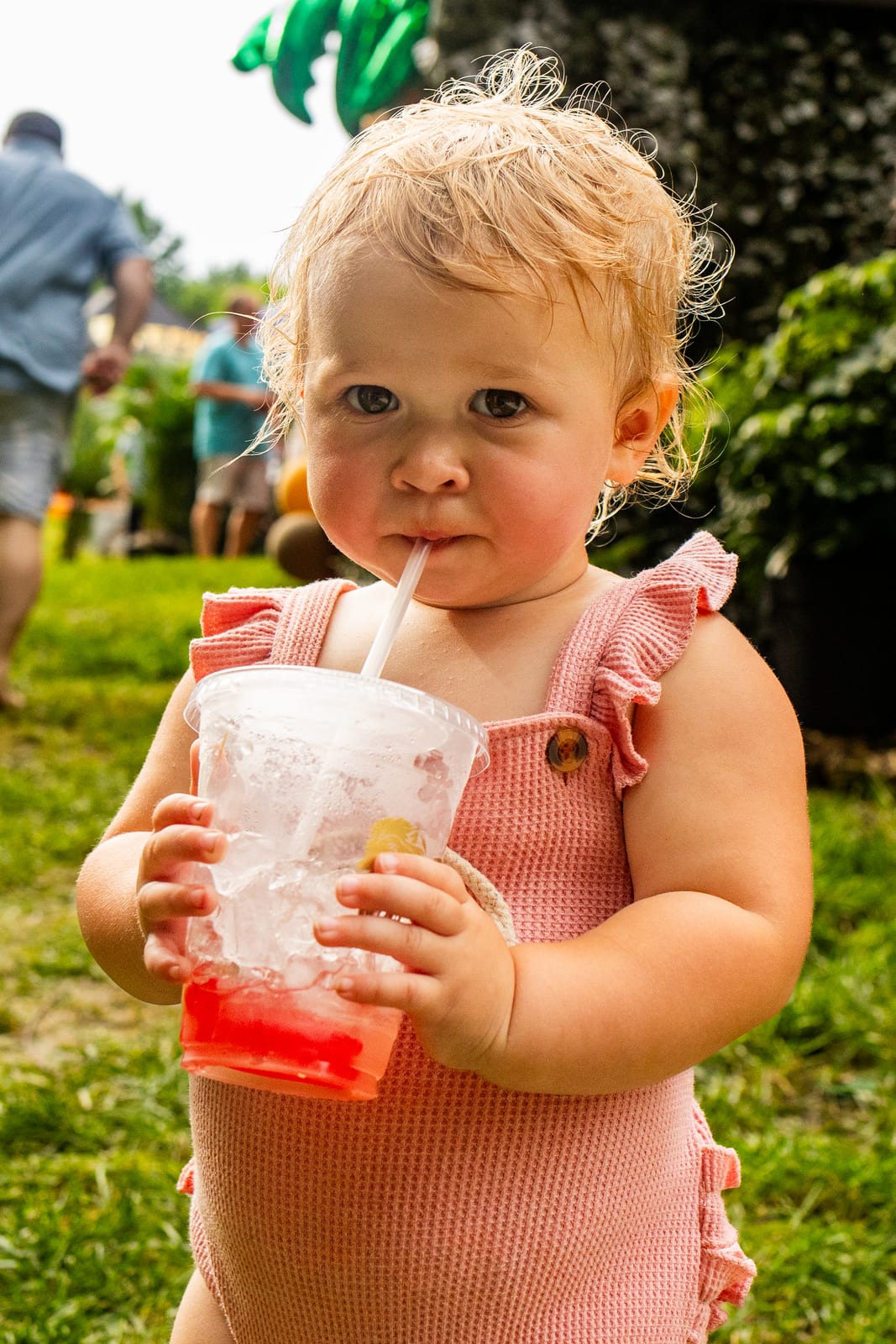 Toddler drinking a frozen fruit drink through a straw on a lawn