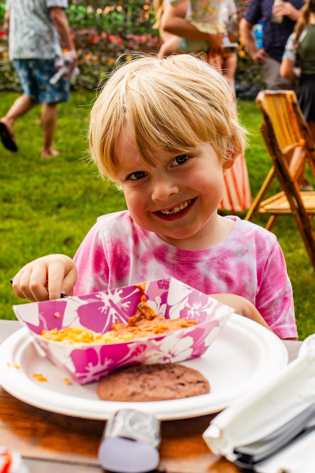 Young guest smiling over a plate of party food at an outdoor table