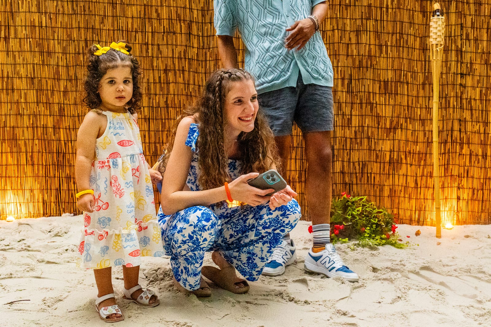 A child and an adult posing together in a sand play area beside tiki torches