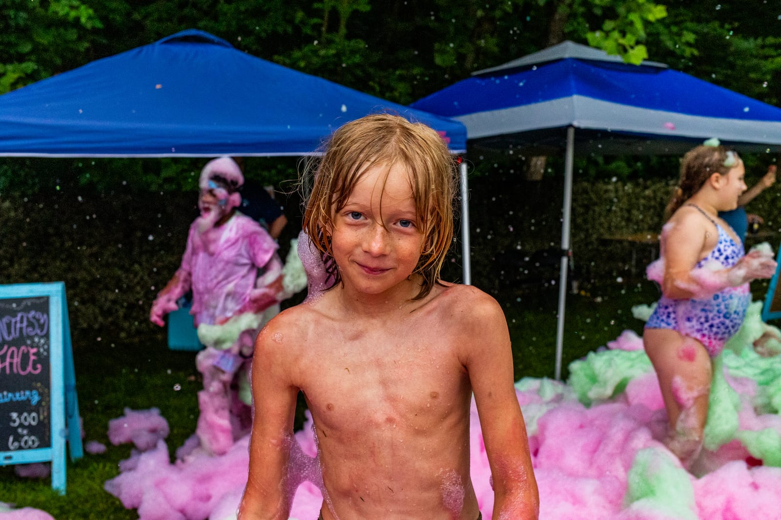 Young guest standing in front of billowing pink foam beneath blue canopies