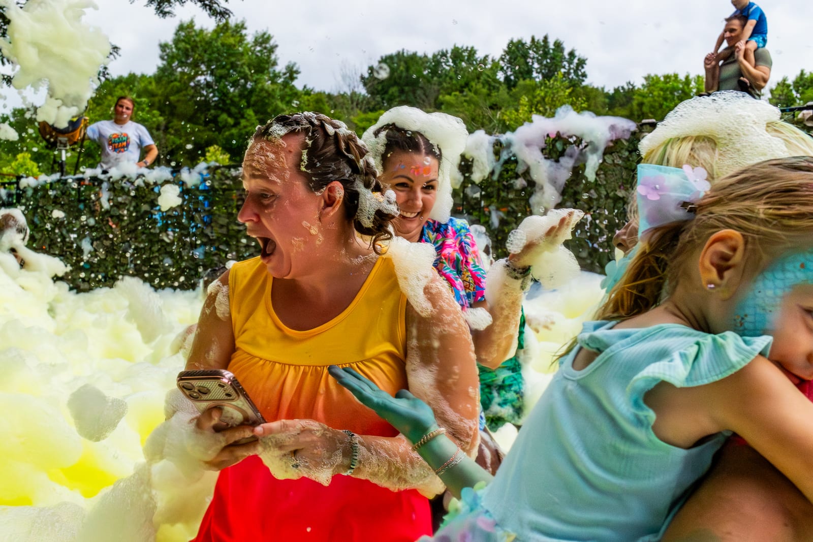 Guests laughing together in white foam at a daytime foam party