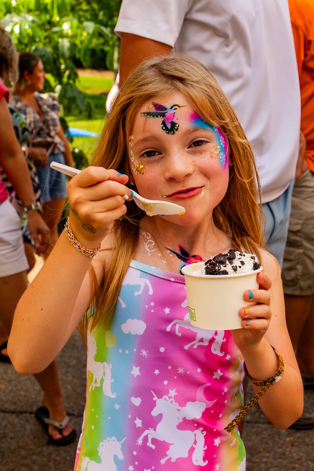 Young guest with glitter face art eating a cup of ice cream