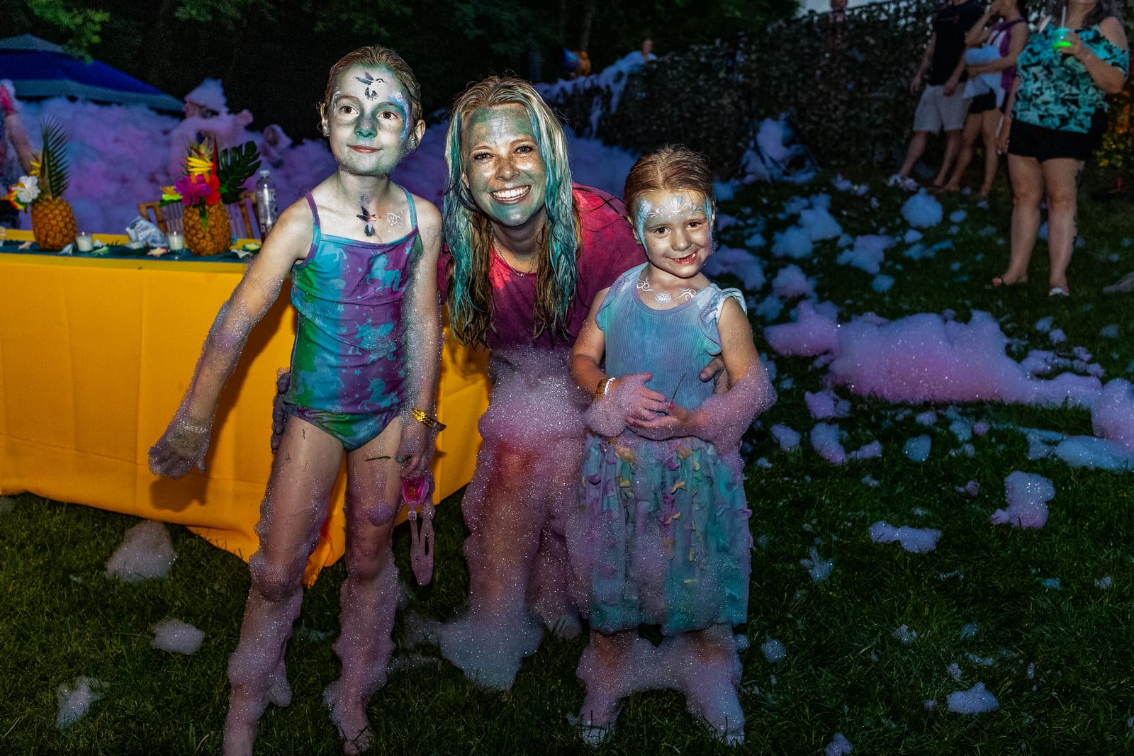 Three young guests covered in foam posing together on a lawn
