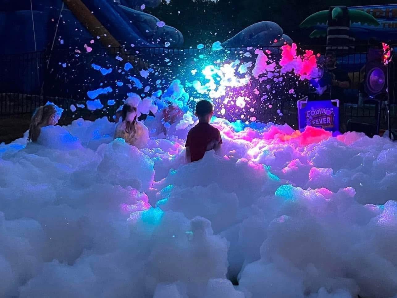 Foam party at night lit in pink and blue with guests silhouetted in the foam