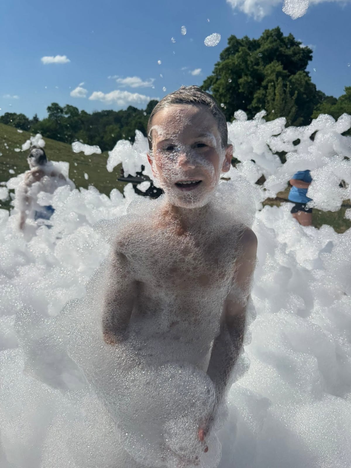 Young guest standing waist deep in white foam on a sunny lawn