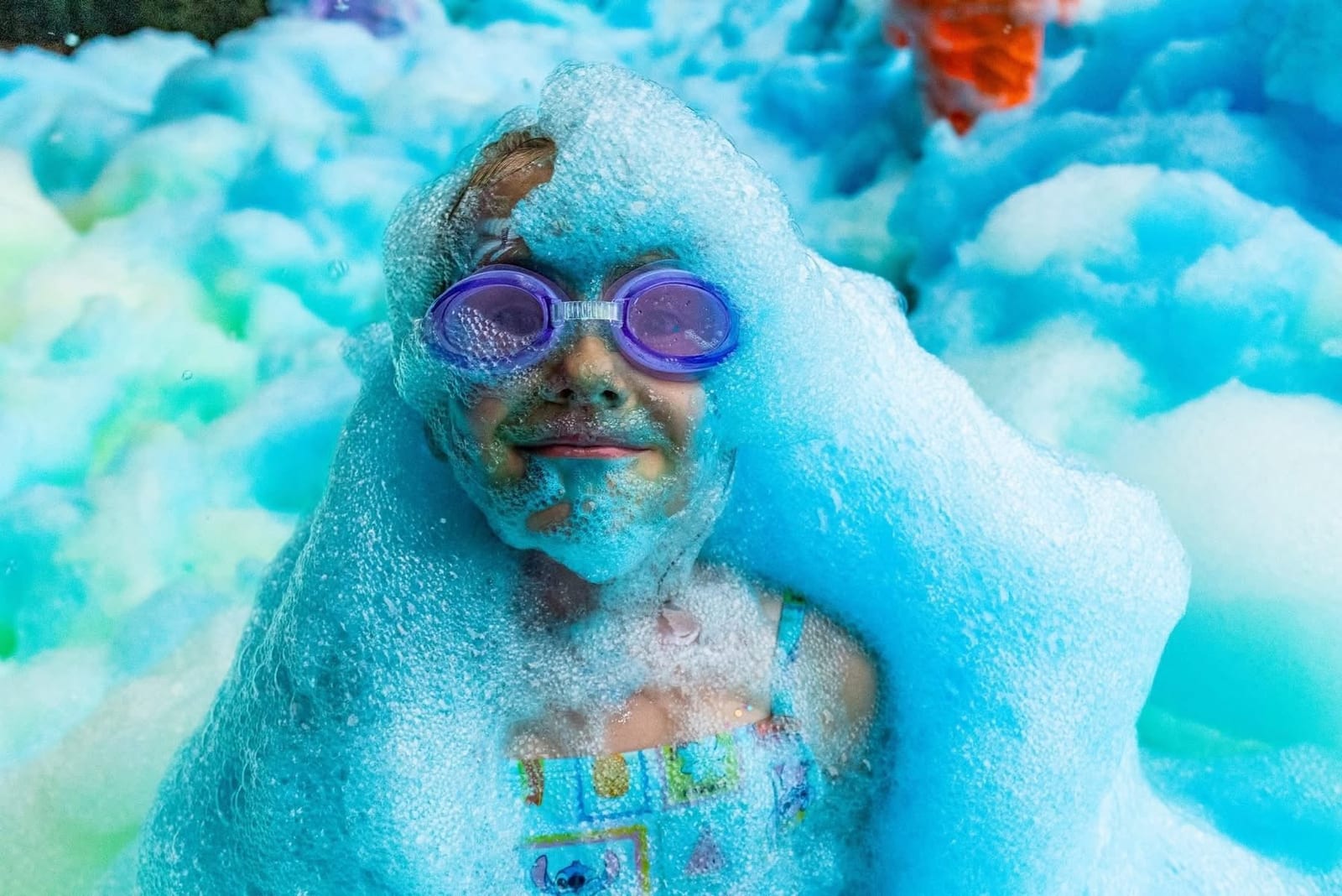 Child in swimming goggles covered head to toe in bright blue foam