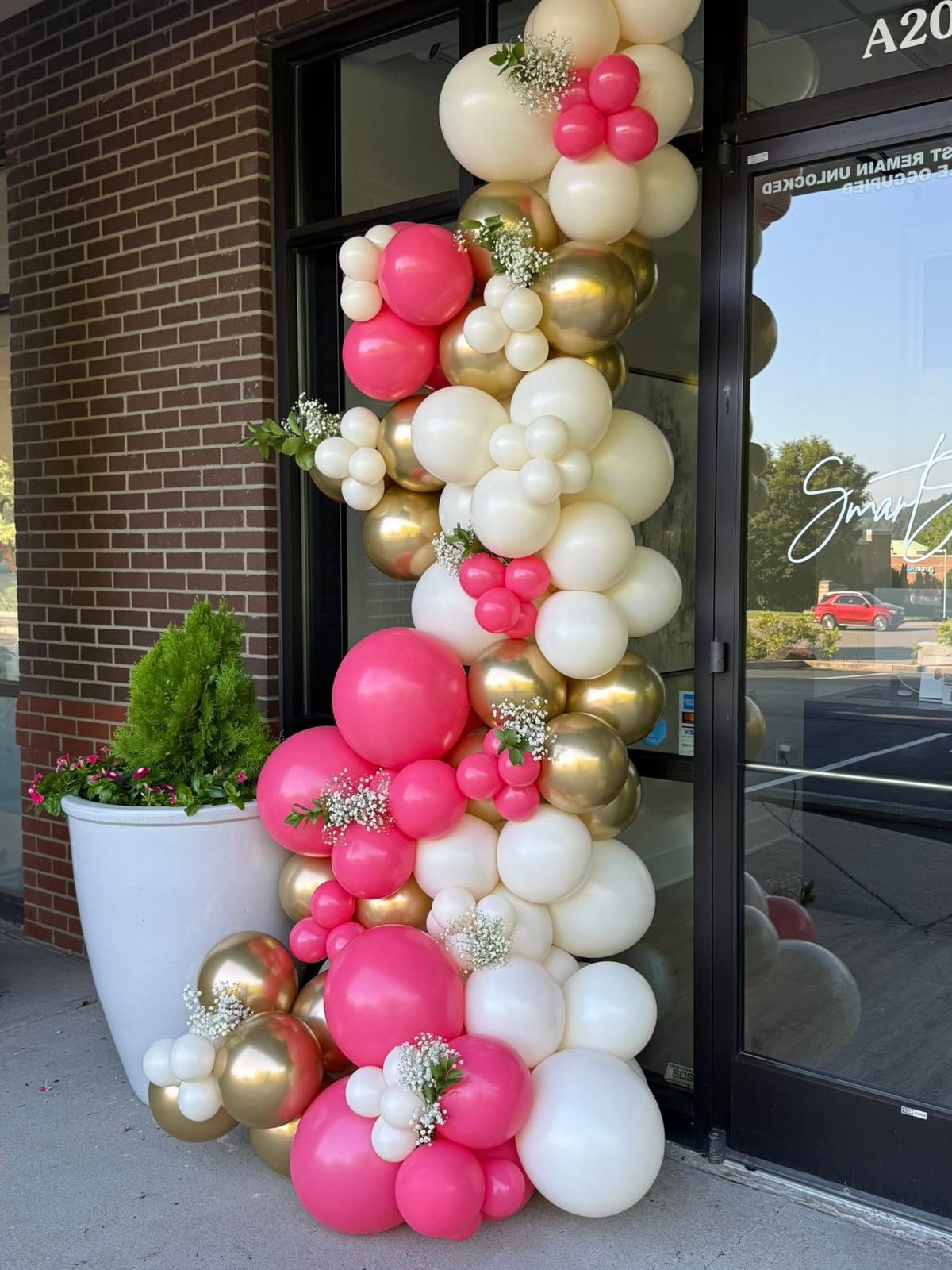 Hot pink, white and gold balloon column framing the glass entrance of a medspa