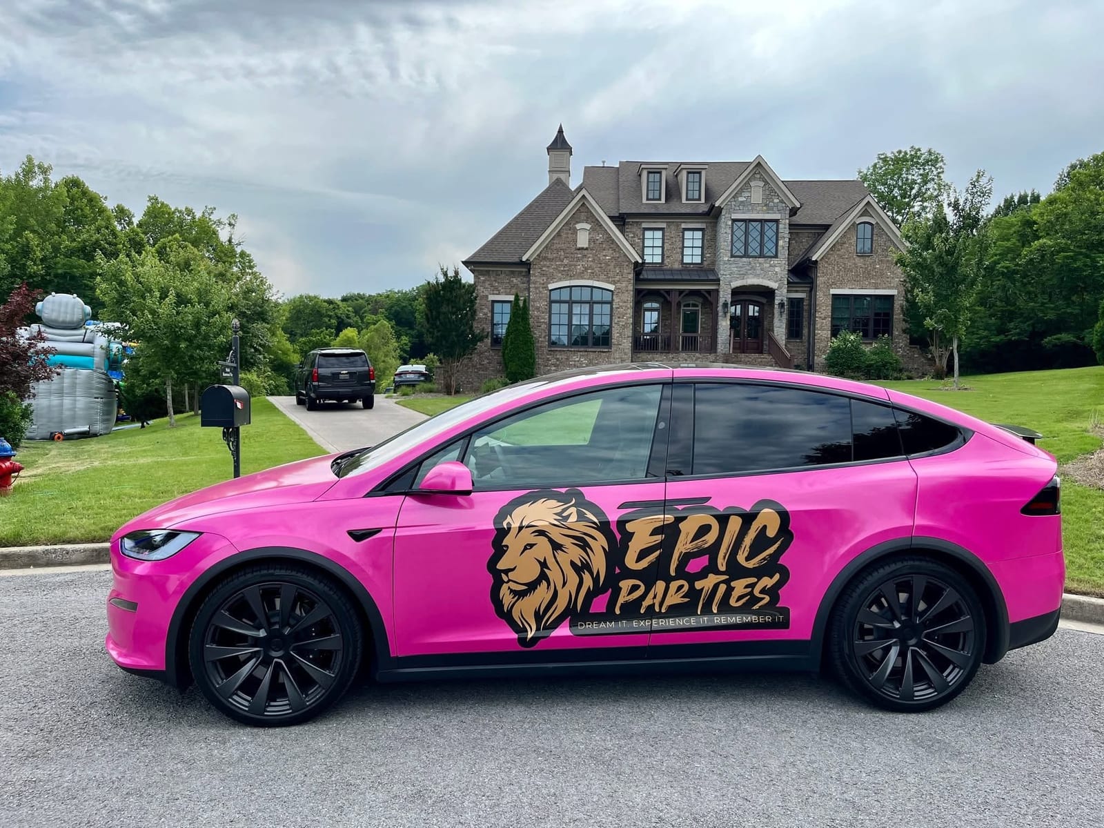 Hot pink EPIC Parties branded SUV with a gold lion logo parked outside a large stone home