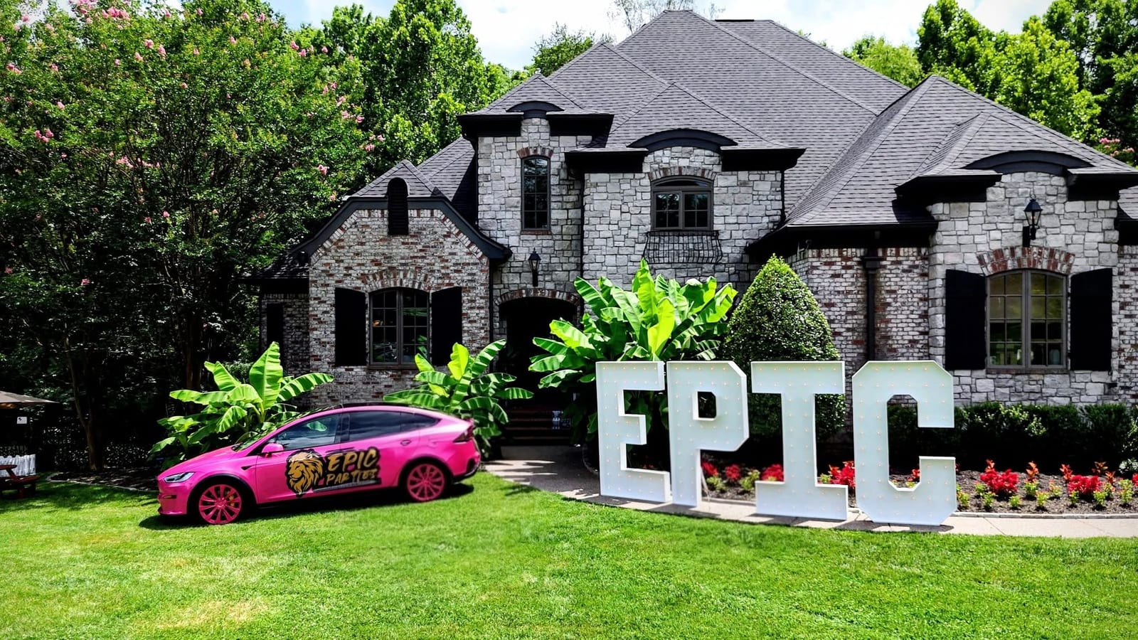 Giant white EPIC marquee letters on a lawn beside a pink branded SUV in front of a stone house