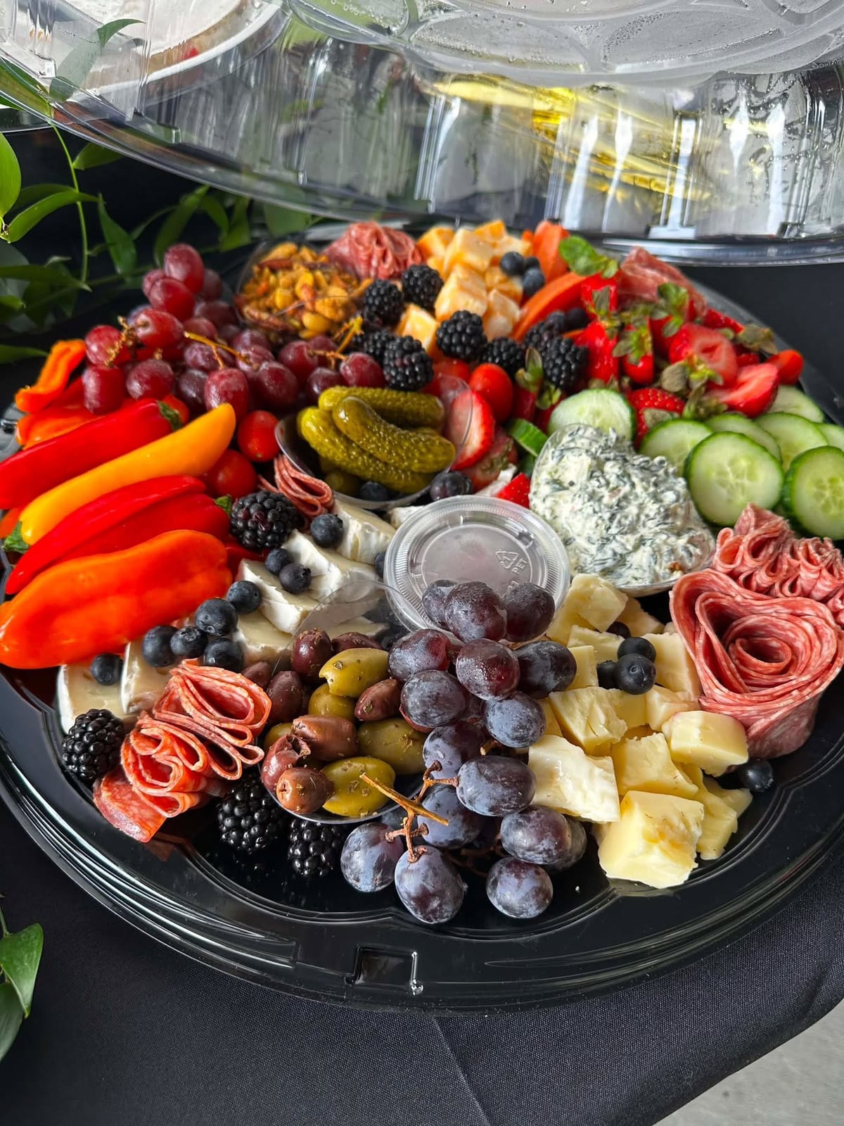 Charcuterie platter of cured meats, cheeses, peppers, grapes and olives under a clear dome