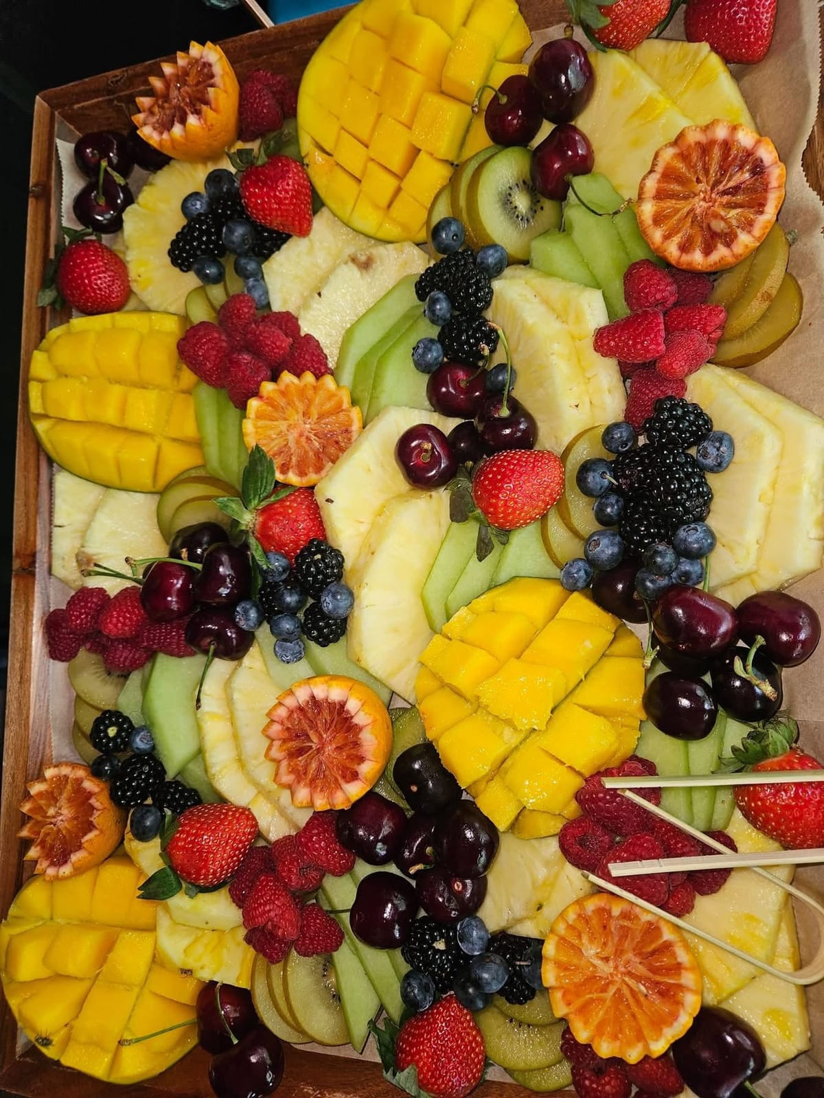 Wooden tray of carved mango, pineapple, cherries, berries and sliced citrus