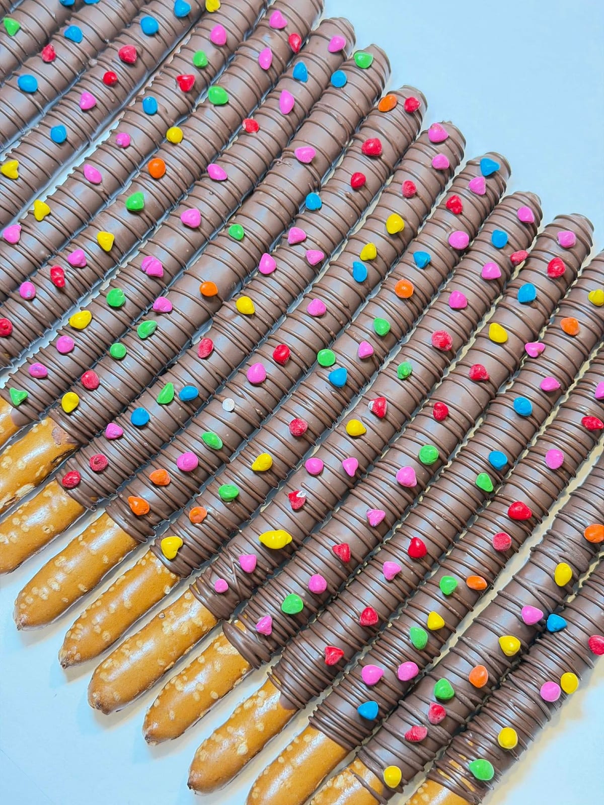 Rows of chocolate-dipped pretzel rods decorated with rainbow candy dots