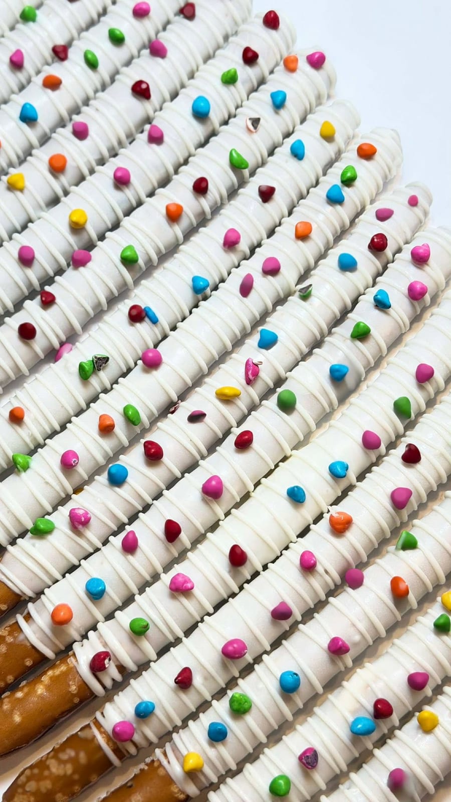 Rows of white chocolate dipped pretzel rods scattered with bright candy dots