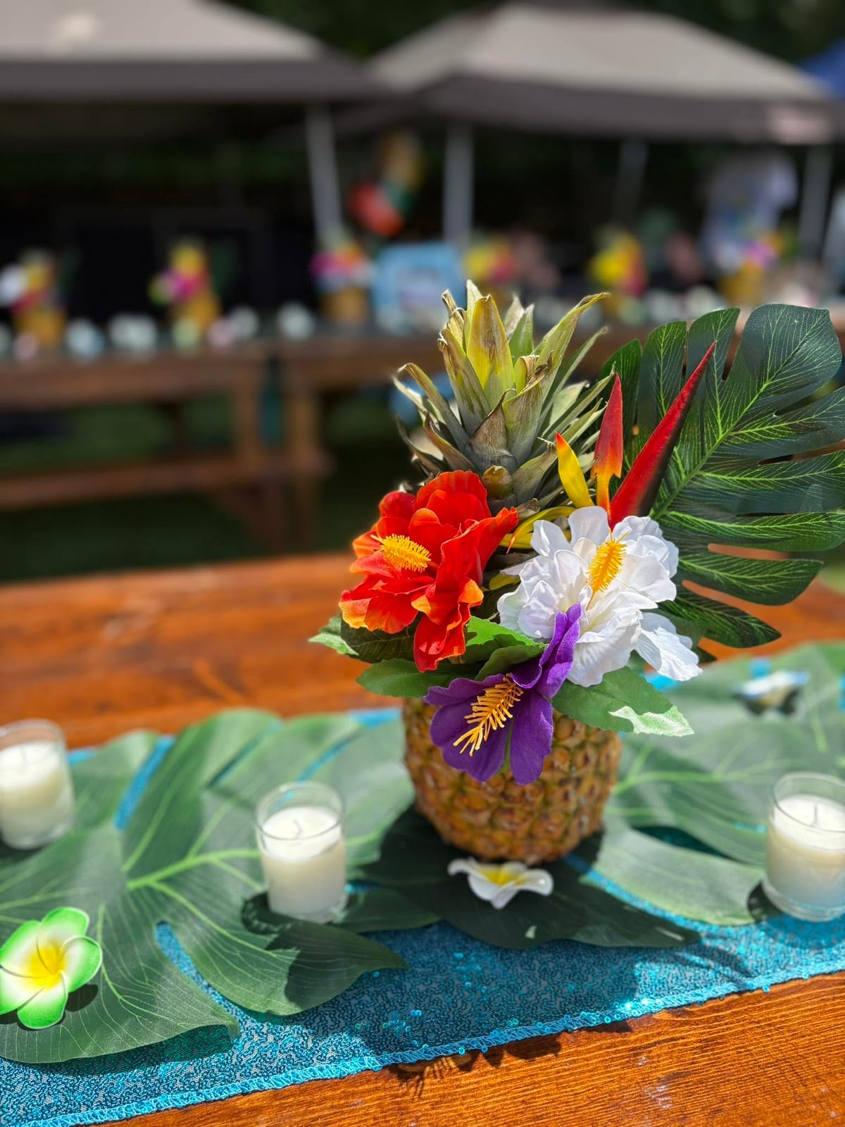 Carved pineapple filled with hibiscus and palm leaves as a centrepiece on a wooden table with candles