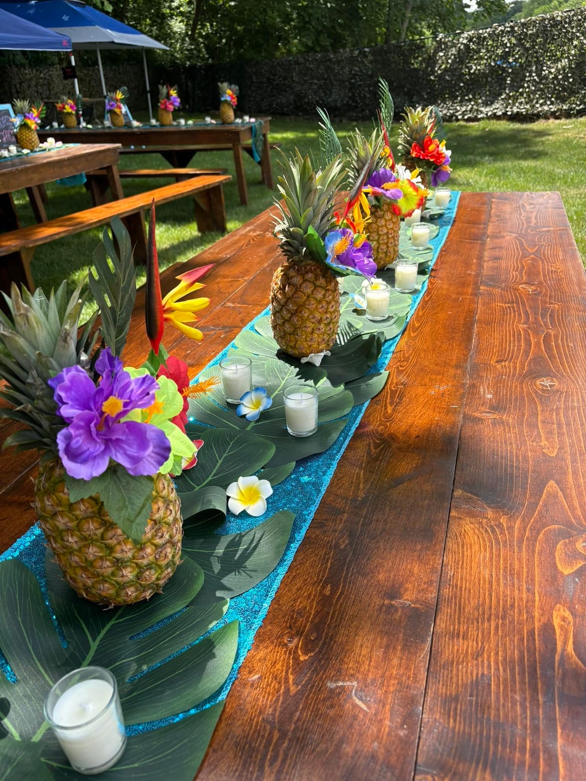 Long wooden banquet table lined with pineapple centrepieces, palm leaf runners and candles