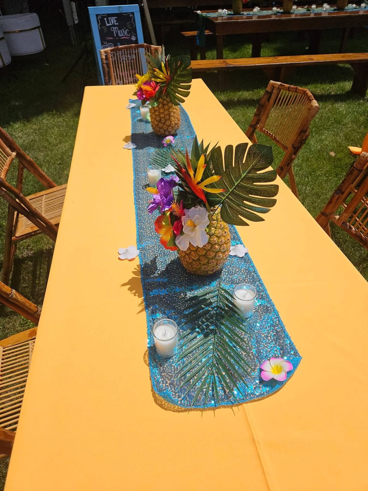 Wooden table dressed with a marigold runner, teal sequin overlay, pineapple centrepiece and candles