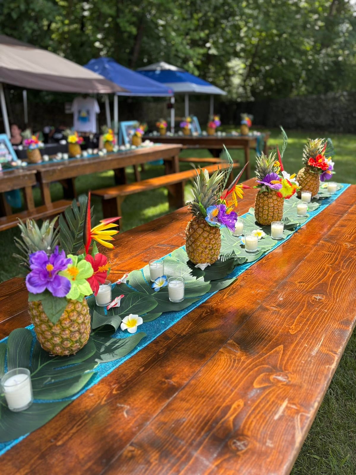 Row of tropical pineapple centrepieces down a long wooden table at an outdoor luau