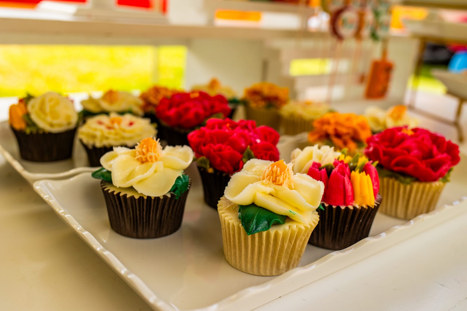 Trays of cupcakes piped as red, yellow and orange buttercream flowers