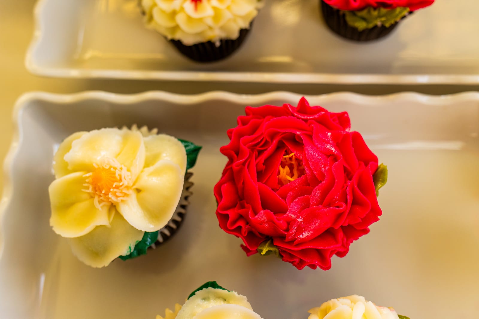 Close-up of cupcakes iced as a yellow blossom and a deep red rose on a scalloped platter