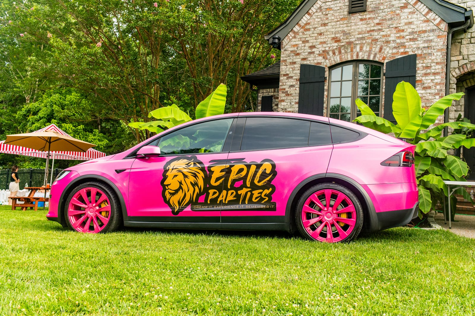 Hot pink EPIC Parties branded car parked on a lawn beside a stone house