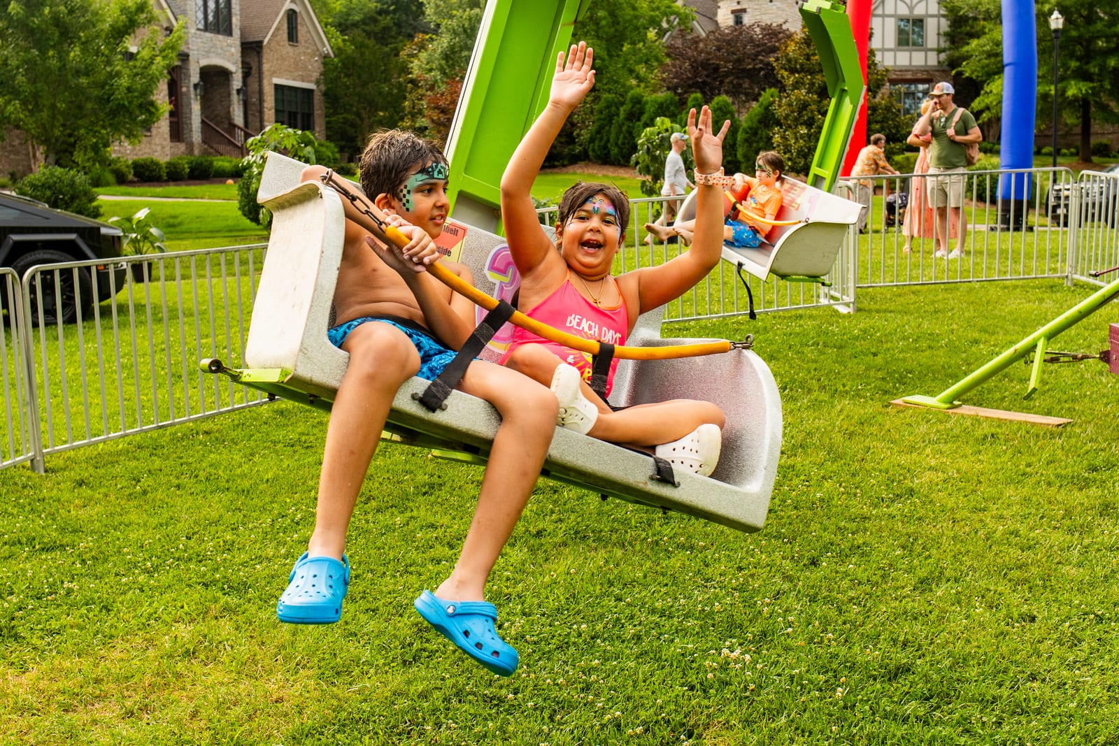 Child on a swing ride with both arms flung overhead, laughing
